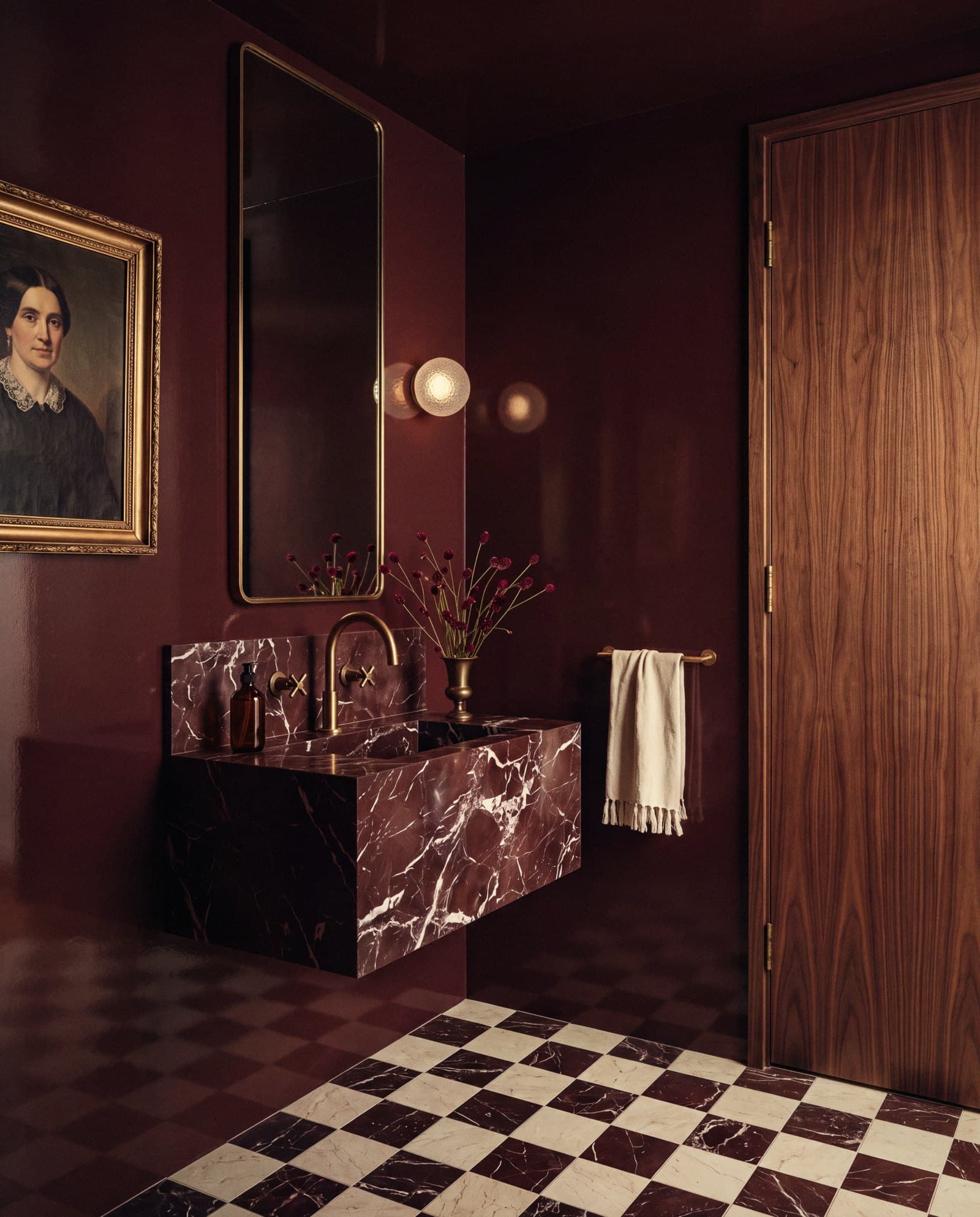 Oxblood lacquered powder room with a red marble basin, brass tap and checkerboard marble floor